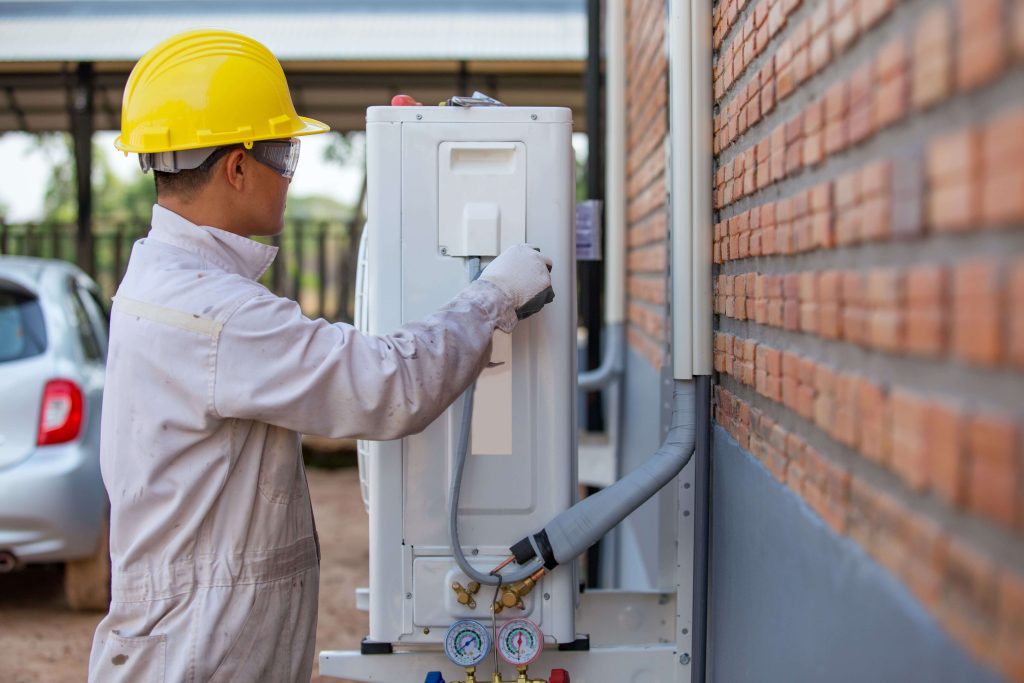 HVAC technician installing an Aprilaire humidifier unit on the side of a home